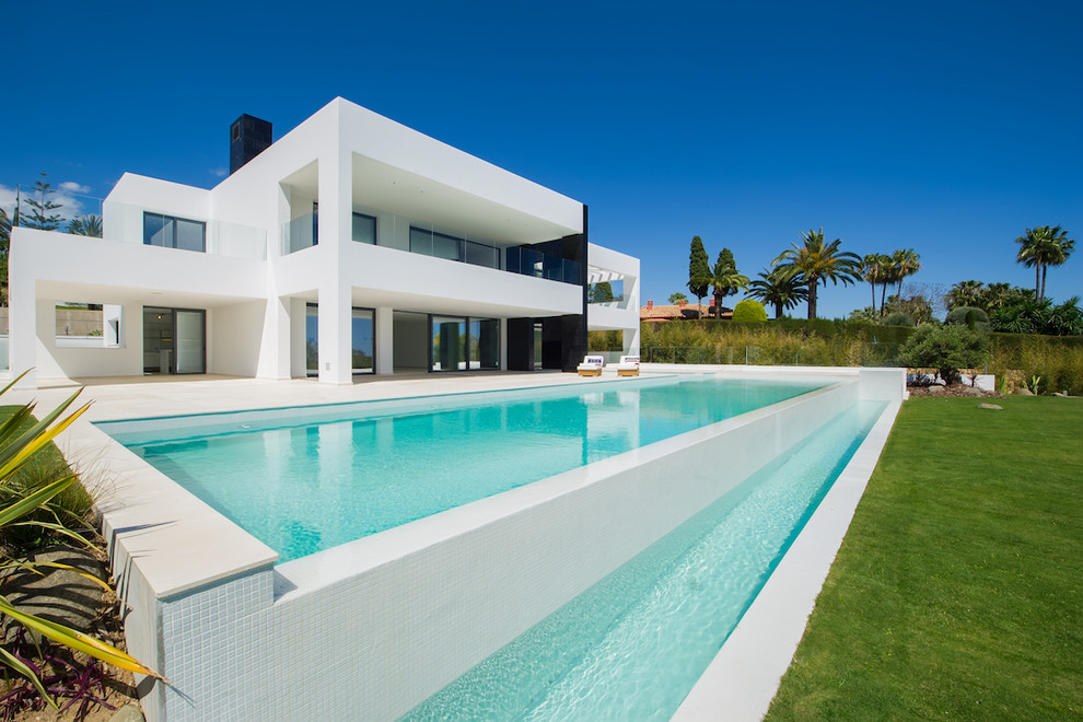 Ejemplo de piscina infinita minimalista rectangular en patio trasero con adoquines de piedra natural
