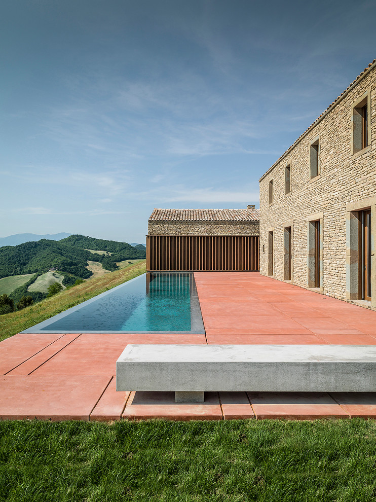 На фото: большой прямоугольный бассейн-инфинити на заднем дворе в средиземноморском стиле с домиком у бассейна и покрытием из бетонных плит