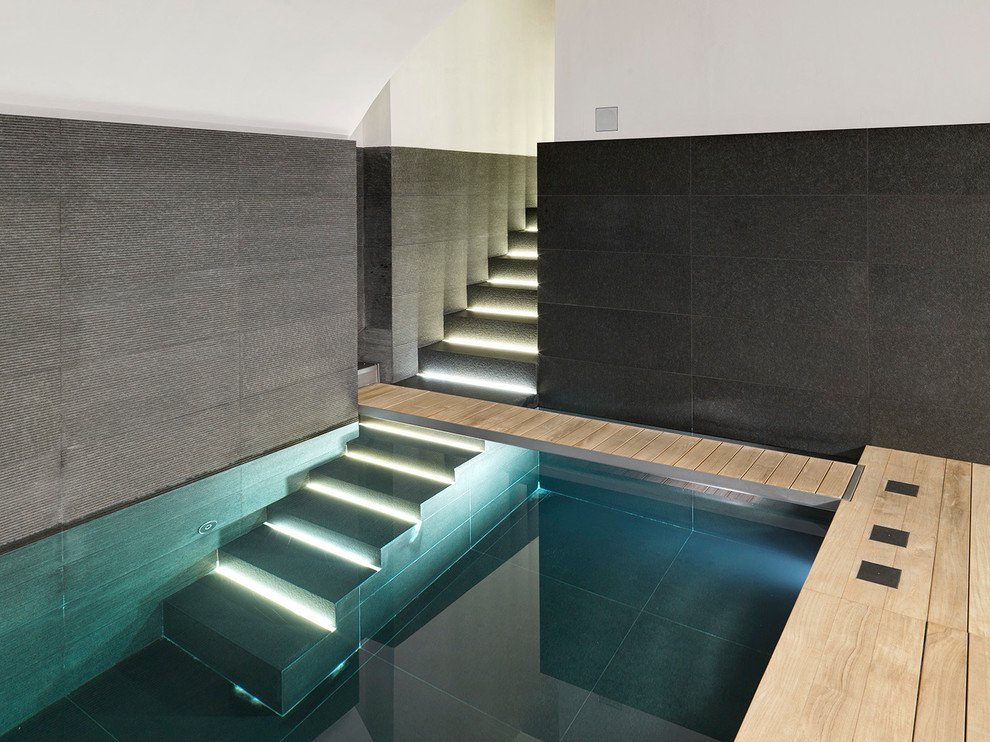 Cette image montre une grande piscine minimaliste rectangle avec un bain bouillonnant et des pavés en pierre naturelle.