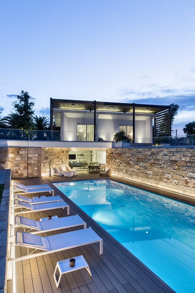 Réalisation d'une piscine à débordement et arrière minimaliste de taille moyenne et rectangle avec une terrasse en bois.