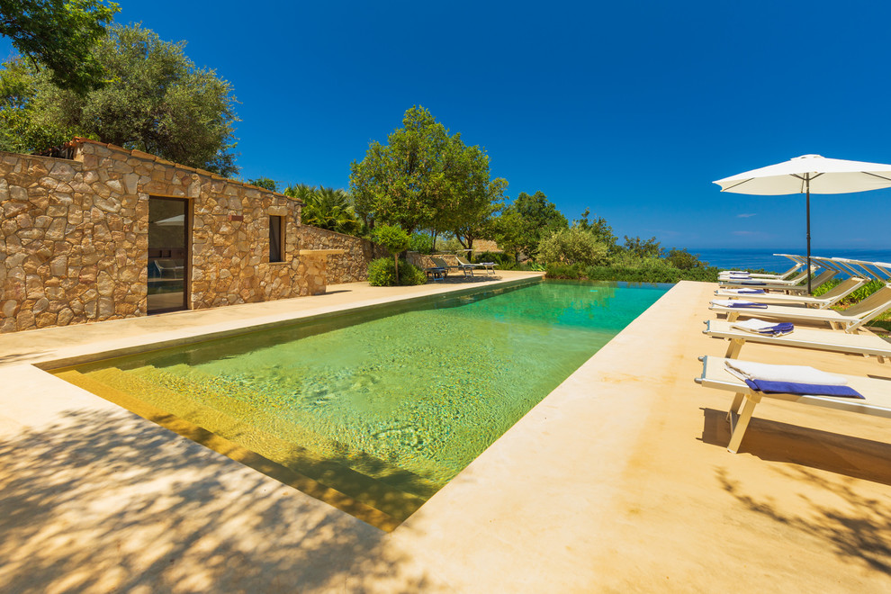 Diseño de piscina infinita mediterránea rectangular en patio trasero con losas de hormigón