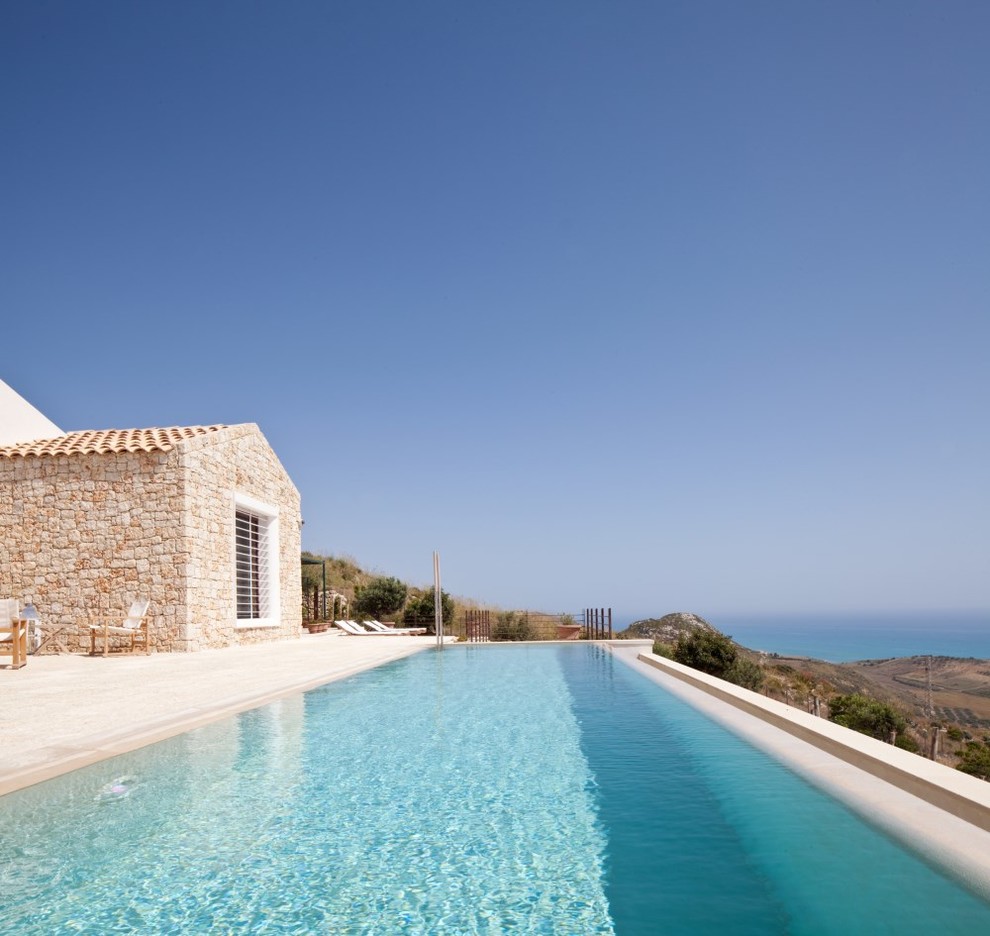 Diseño de piscina infinita mediterránea en forma de L en patio trasero con adoquines de piedra natural