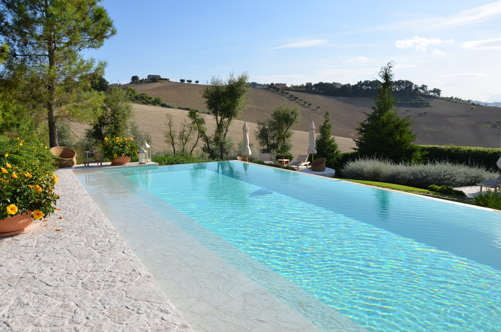 Ejemplo de piscina infinita de estilo de casa de campo rectangular con adoquines de piedra natural