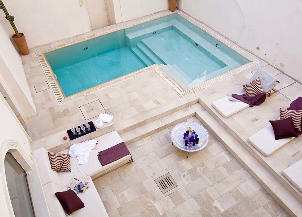 Réalisation d'une piscine à débordement et latérale méditerranéenne en L de taille moyenne avec un bain bouillonnant et des pavés en pierre naturelle.
