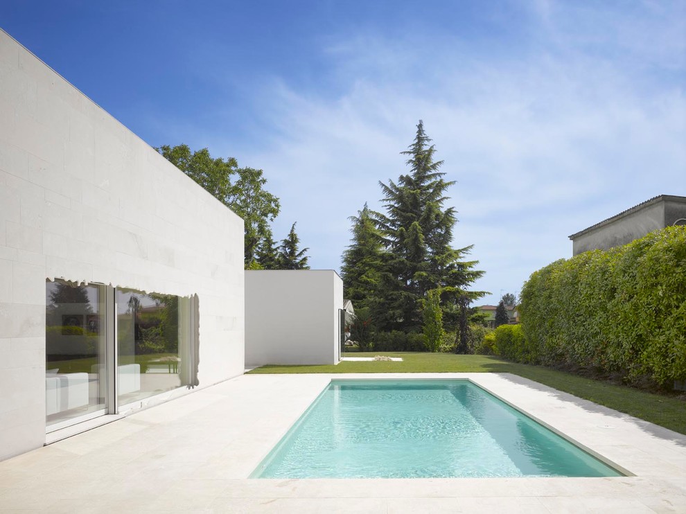 Contemporary side rectangular swimming pool in Milan with natural stone paving.