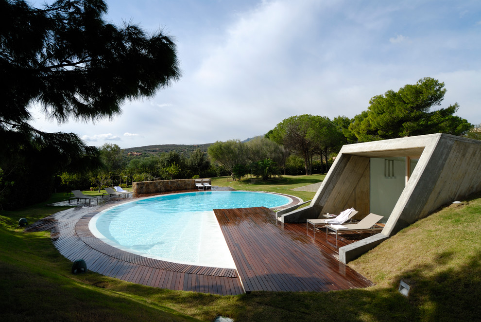 Large contemporary custom shaped swimming pool in Other with a pool house and decking.