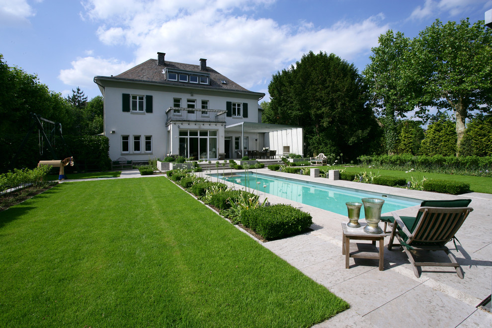 Modelo de piscina alargada clásica grande rectangular en patio trasero con suelo de baldosas