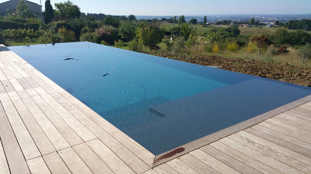 Réalisation d'une grande piscine à débordement et arrière design rectangle avec une terrasse en bois.