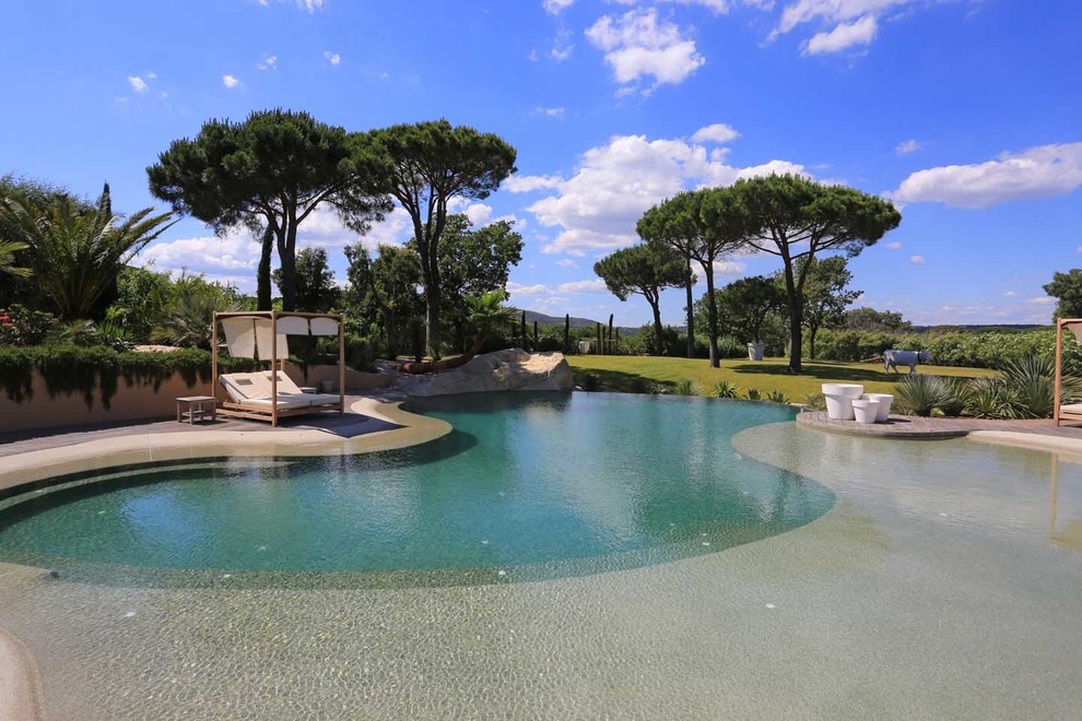 Aménagement d'une grande piscine naturelle méditerranéenne sur mesure avec une terrasse en bois.