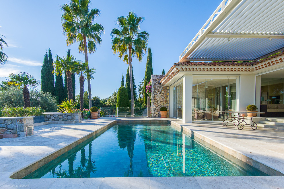 Réalisation d'une grande piscine arrière méditerranéenne rectangle avec des pavés en pierre naturelle.