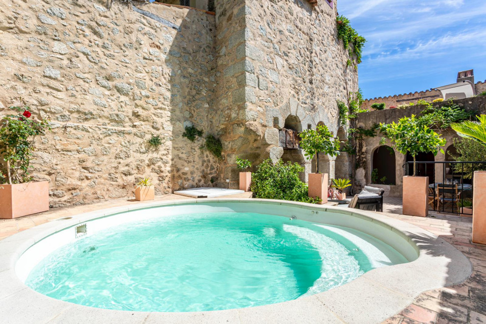 Exemple d'une petite piscine éclectique ronde avec un bain bouillonnant, une cour et des pavés en pierre naturelle.