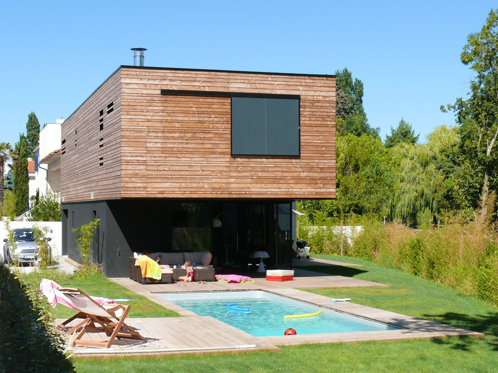 Réalisation d'une piscine latérale design de taille moyenne et rectangle avec une terrasse en bois.