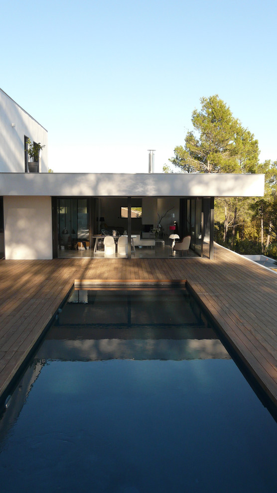 Cette image montre une piscine arrière minimaliste de taille moyenne et rectangle avec une terrasse en bois.