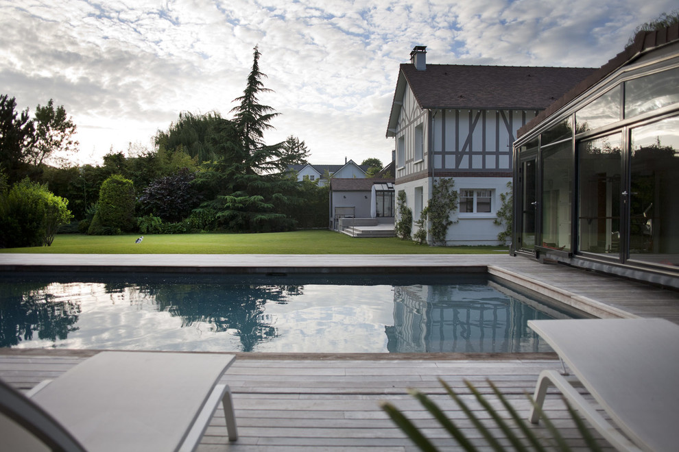 Exemple d'un grand piscine avec aménagement paysager arrière chic rectangle avec une terrasse en bois.