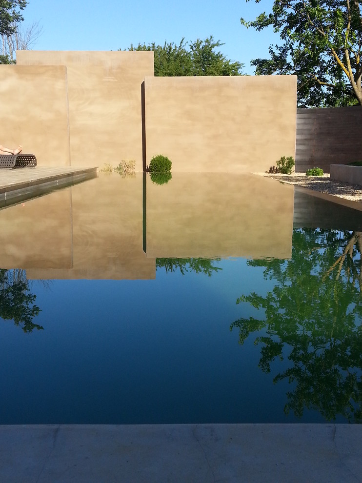 Exemple d'une grande piscine à débordement tendance rectangle avec une terrasse en bois.