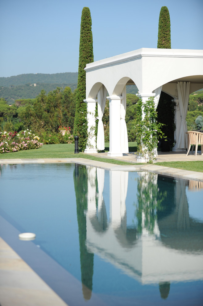 Ejemplo de casa de la piscina y piscina alargada mediterránea de tamaño medio a medida en patio trasero con adoquines de piedra natural
