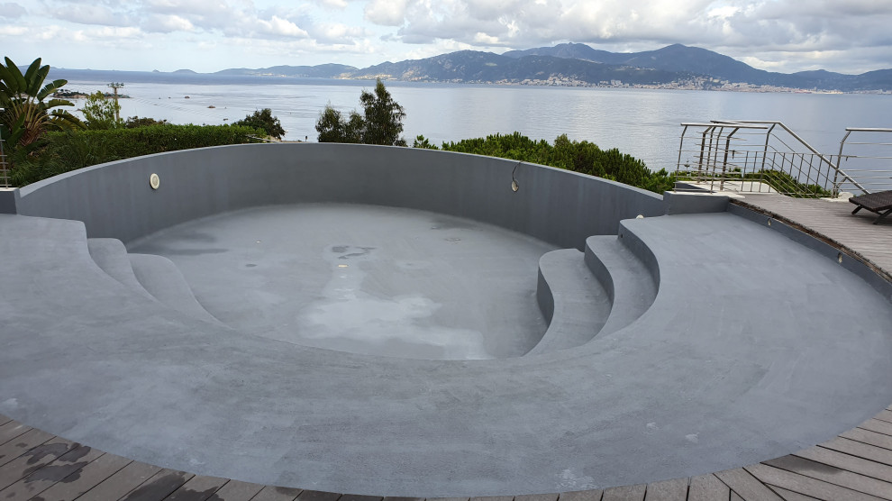 Inspiration pour une grande piscine à débordement et arrière design ronde avec une terrasse en bois.