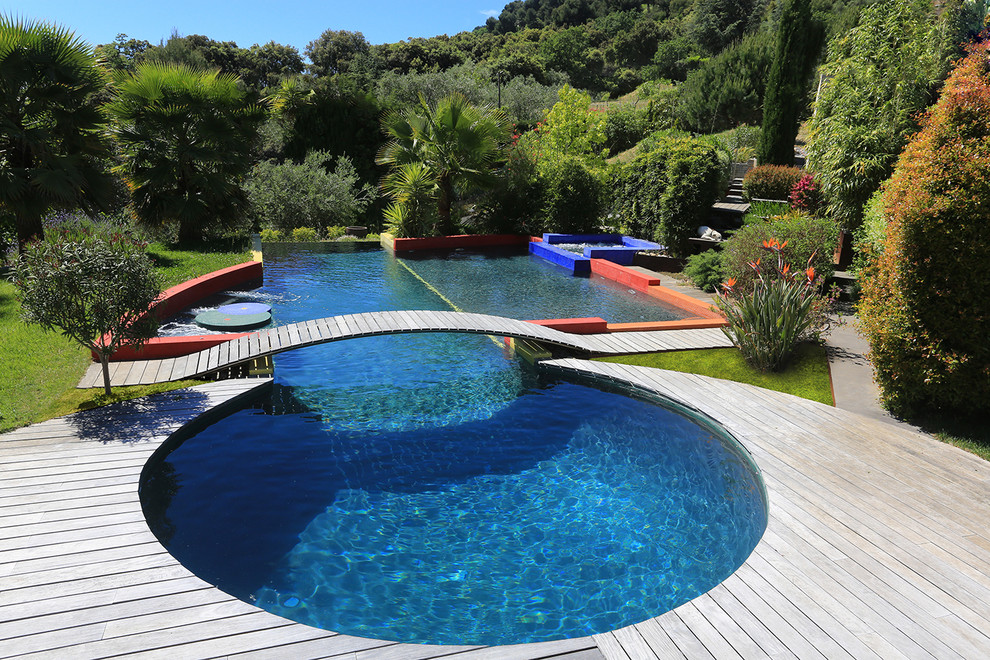 Réalisation d'une grande piscine arrière design sur mesure avec un bain bouillonnant et une terrasse en bois.