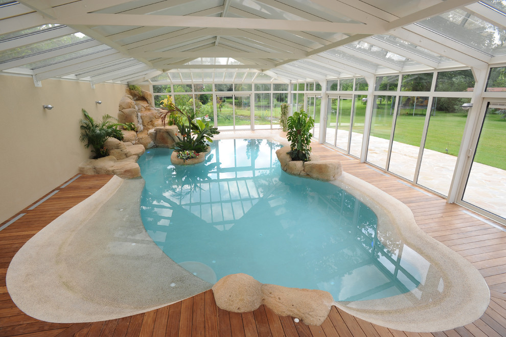 Exotisk inredning av en mellanstor inomhus, anpassad pool, med trädäck och poolhus