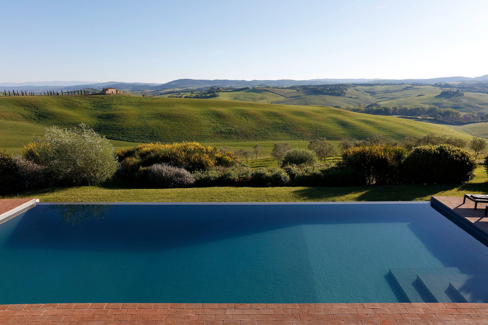 Immagine di una piscina a sfioro infinito moderna rettangolare dietro casa con pavimentazioni in mattoni