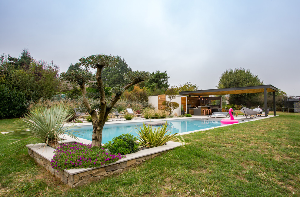 Imagen de piscina alargada actual grande rectangular en patio trasero con adoquines de piedra natural