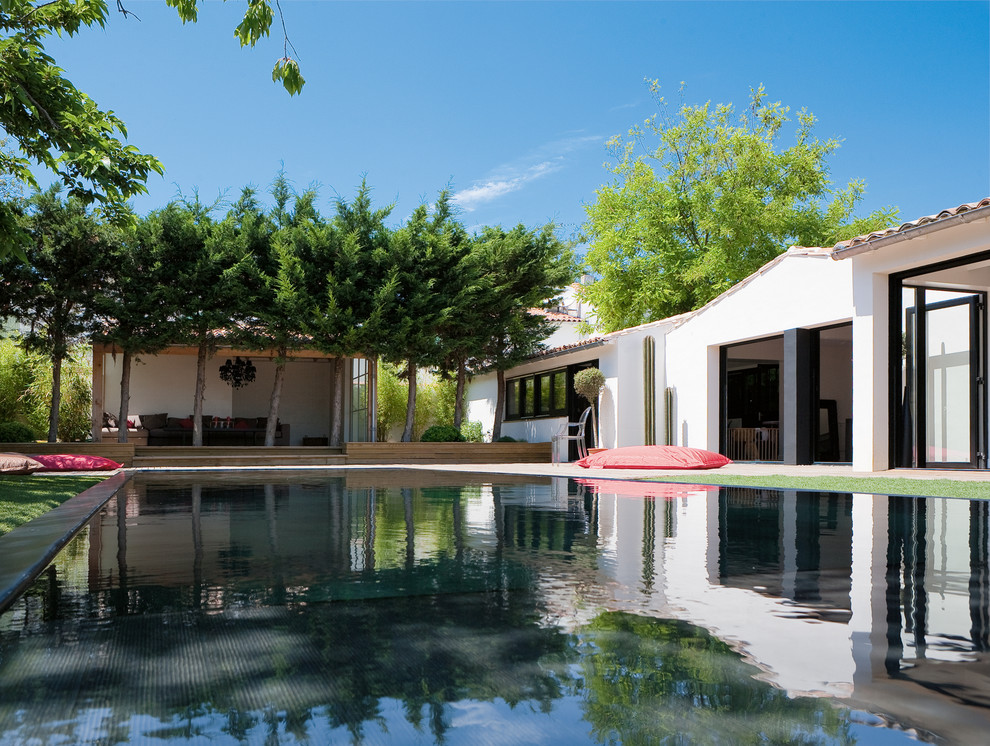 Expansive contemporary back rectangular swimming pool in Other with a pool house and decking.