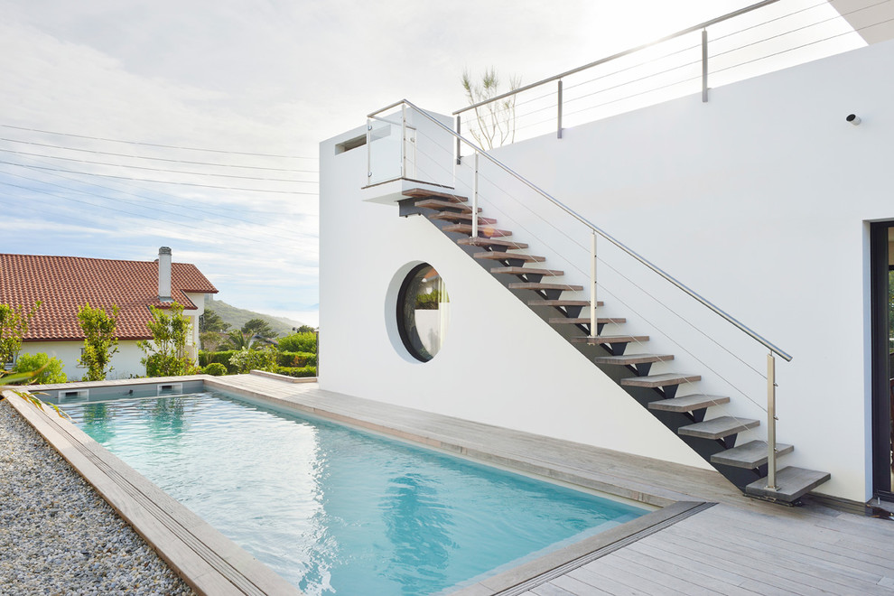 Diseño de piscina alargada, minimalista, grande, rectangular, en patio lateral, con entablado