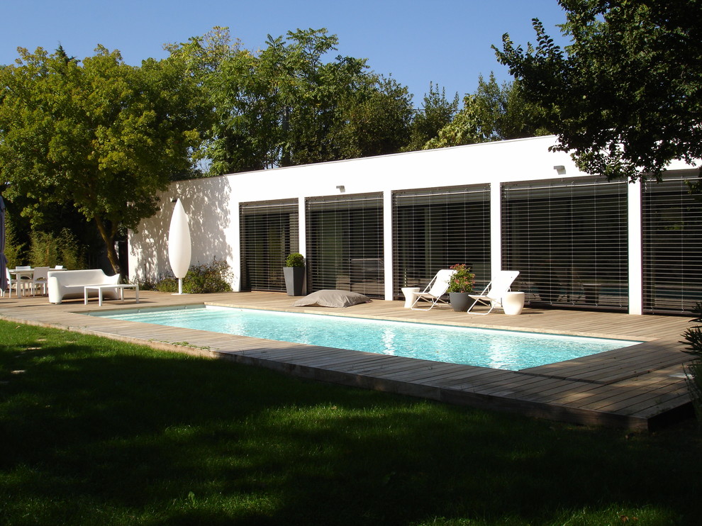 Exempel på en mellanstor modern rektangulär pool på baksidan av huset, med trädäck