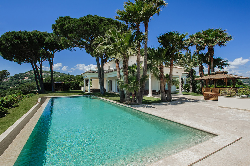 Imagen de casa de la piscina y piscina alargada exótica grande rectangular en patio trasero con suelo de baldosas