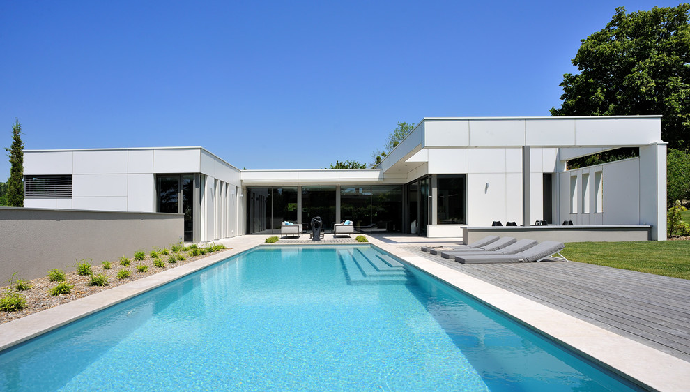 Идея дизайна: большой прямоугольный бассейн на заднем дворе в стиле модернизм с настилом
