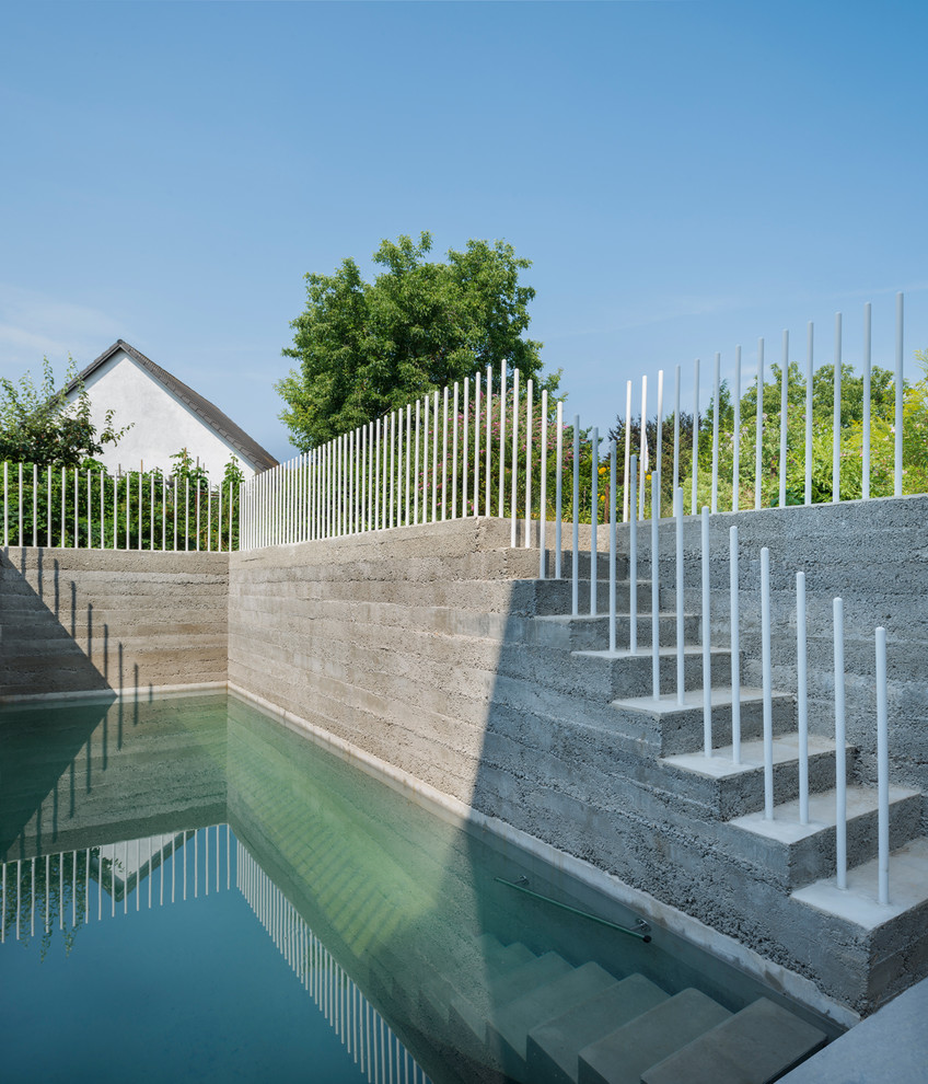 Ejemplo de piscina actual de tamaño medio rectangular en patio trasero con adoquines de hormigón