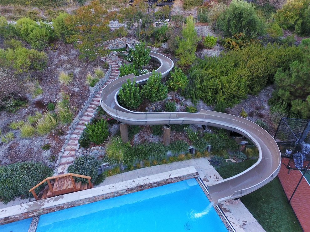 Modelo de piscina con tobogán natural clásica grande a medida en patio trasero con suelo de hormigón estampado