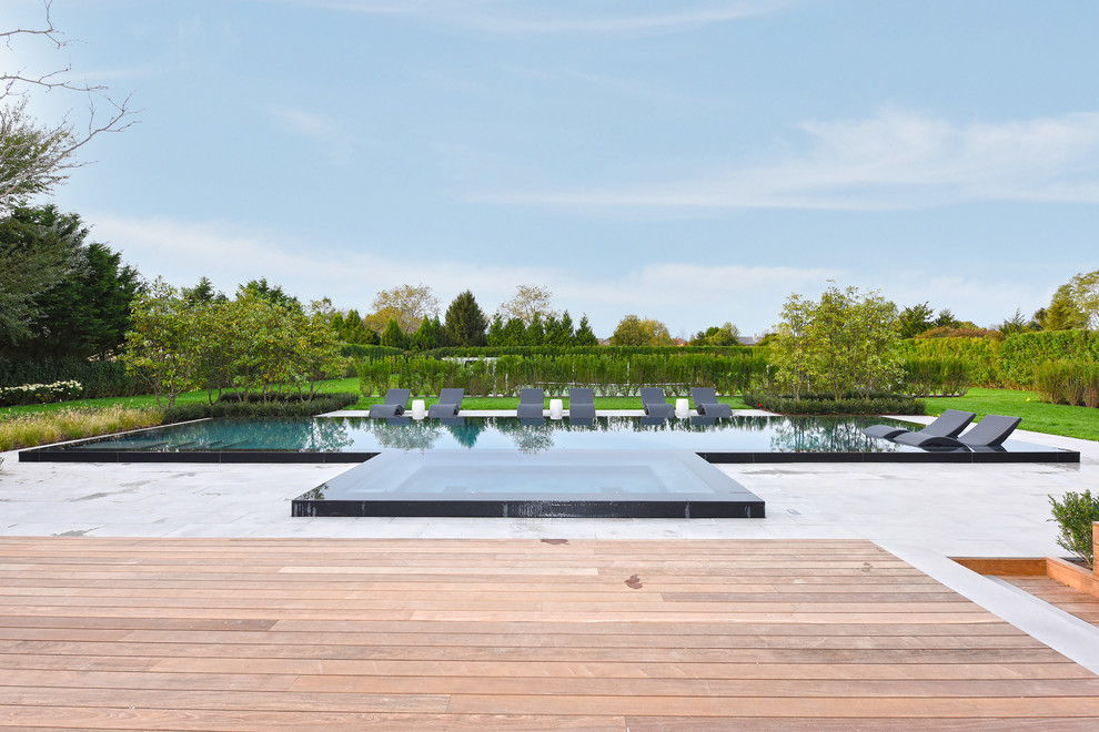 Photo of an expansive contemporary back custom shaped infinity swimming pool in New York with a pool house and tiled flooring.