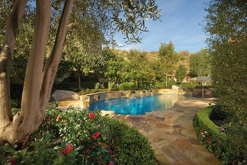 Large mediterranean back custom shaped lengths swimming pool in Orange County with a water feature and natural stone paving.