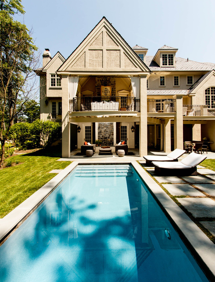 Modelo de piscina clásica renovada grande rectangular en patio trasero con adoquines de piedra natural