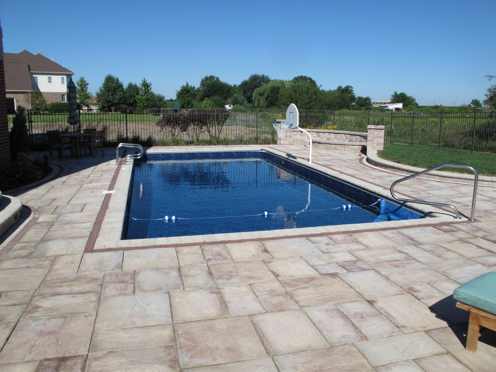 Imagen de piscina tradicional de tamaño medio rectangular en patio trasero con adoquines de piedra natural