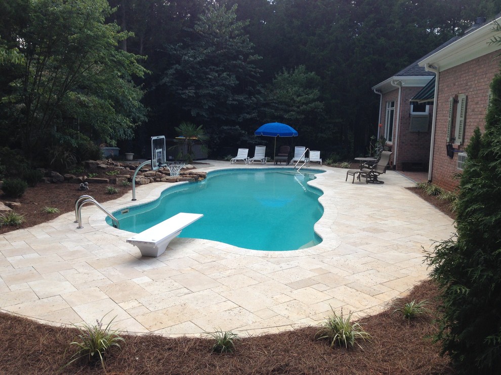 Aménagement d'une grande piscine arrière exotique sur mesure avec un point d'eau et des pavés en pierre naturelle.