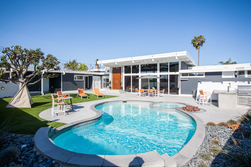 Idee per una piscina moderna a "C" dietro casa con una vasca idromassaggio e pavimentazioni in cemento