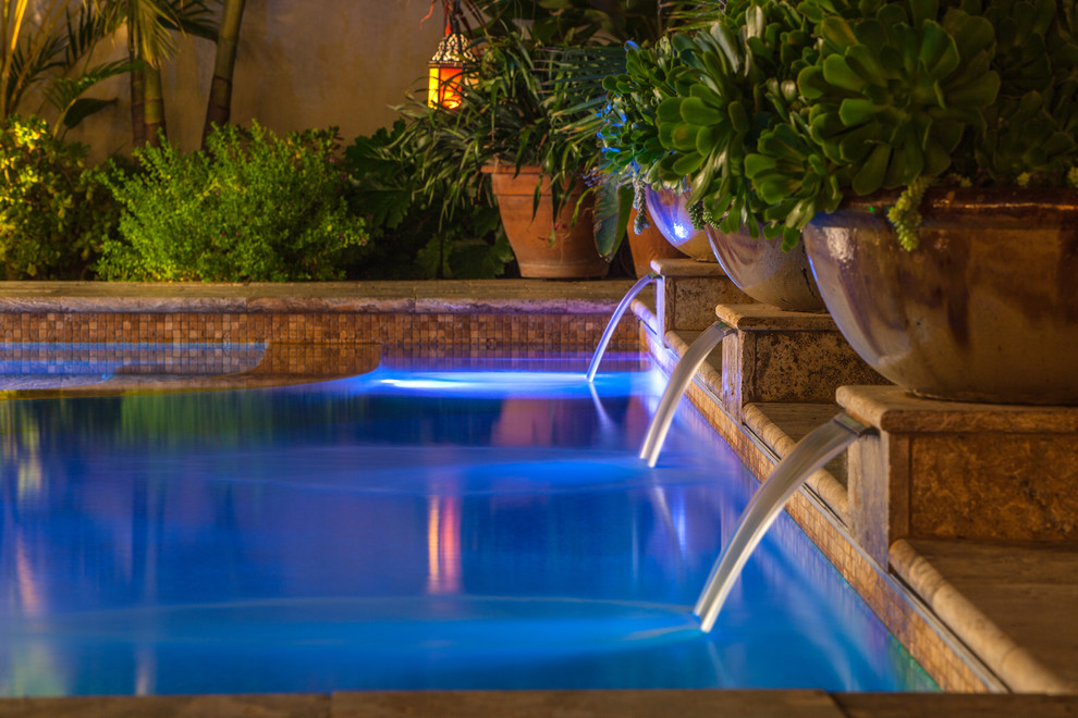 Photo of a large mediterranean back rectangular lengths swimming pool in San Diego with a water feature and natural stone paving.