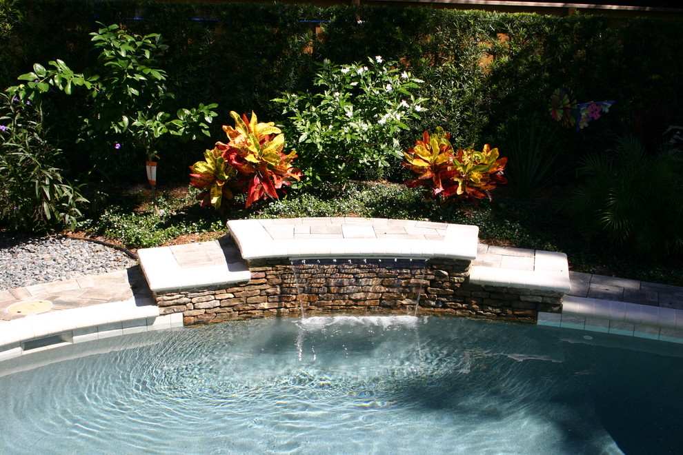 Diseño de piscina con fuente tropical de tamaño medio a medida en patio trasero con adoquines de hormigón