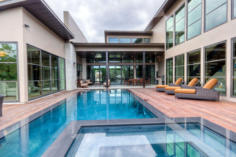 Réalisation d'une piscine à débordement design rectangle avec une cour, une terrasse en bois et un bain bouillonnant.