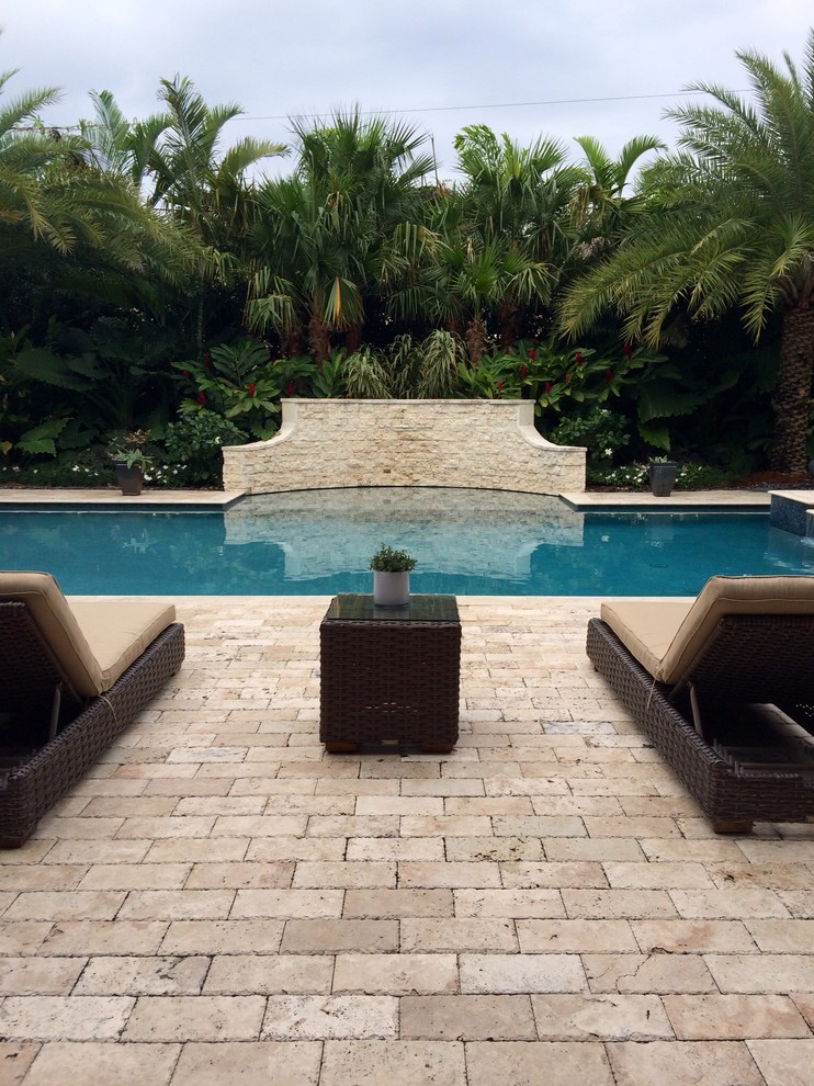 Ejemplo de piscina con fuente natural tropical grande rectangular en patio trasero con adoquines de piedra natural