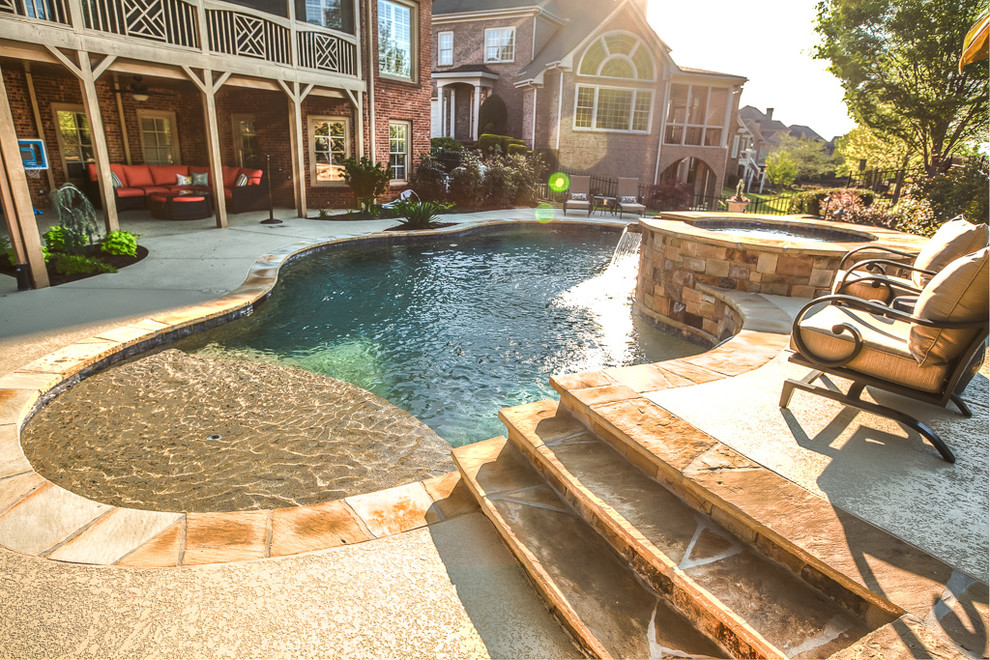 Idee per una grande piscina naturale stile americano personalizzata dietro casa con fontane e cemento stampato