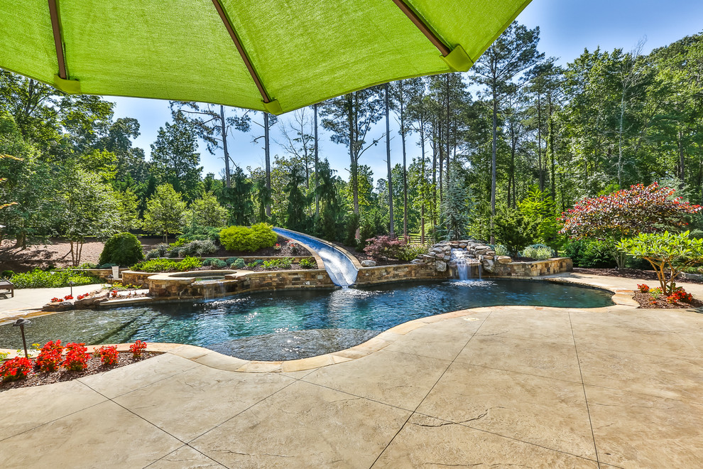Cette photo montre une grande piscine naturelle et arrière exotique sur mesure avec un toboggan et une terrasse en bois.