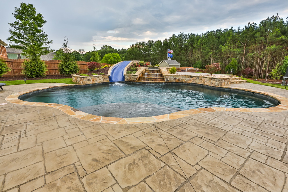 Modelo de piscina con tobogán natural clásica de tamaño medio a medida en patio trasero con suelo de hormigón estampado