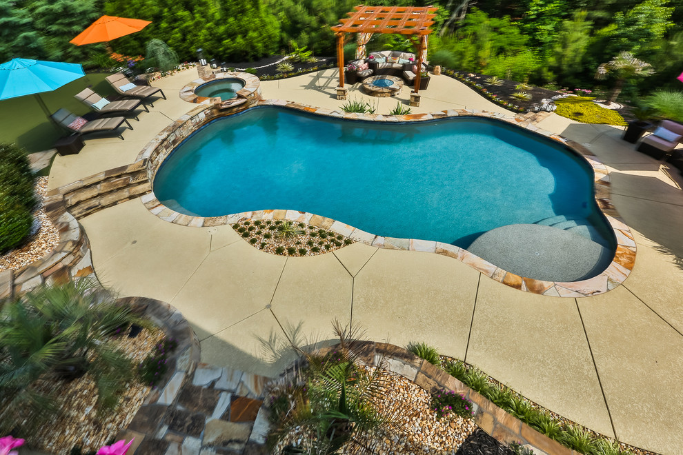 Immagine di una grande piscina naturale classica personalizzata dietro casa con fontane e lastre di cemento