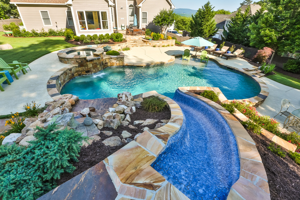 Modelo de piscina con tobogán natural tradicional grande a medida en patio trasero con losas de hormigón