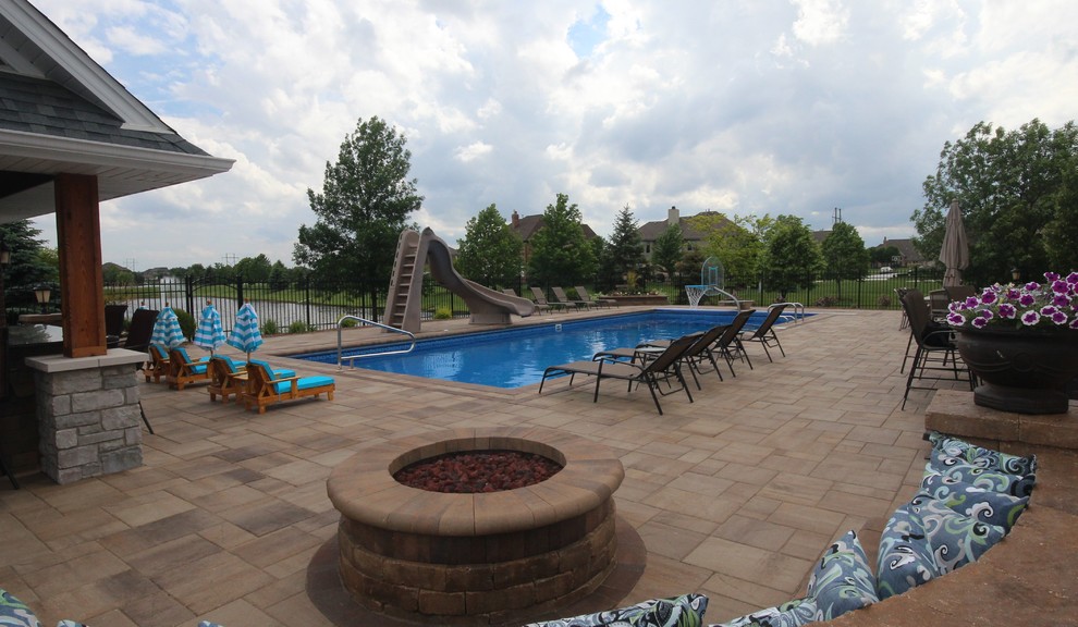 Modelo de piscina con tobogán alargada clásica grande rectangular en patio trasero con adoquines de ladrillo