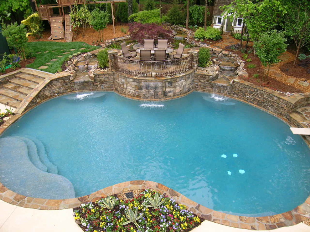 Immagine di una grande piscina naturale tradizionale personalizzata dietro casa con fontane e pavimentazioni in pietra naturale