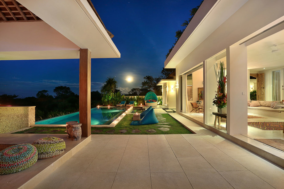 Foto di una grande piscina a sfioro infinito tropicale rettangolare dietro casa con una dépendance a bordo piscina e pavimentazioni in pietra naturale